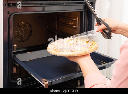 Removing the packaging from the pizza before placing it in the oven Stock Photo
