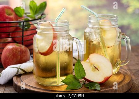 Two glasses of cold apple juice on a wooden platter with rural summer background Stock Photo