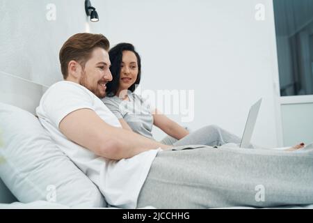 Young couple sitting in bed with laptop Stock Photo