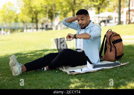 Young male freelance programmer feeling shocked from overtime for doing job via laptop computer, sitting in park Stock Photo