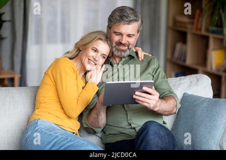 Technologies For Leisure. Happy Middle Aged Spouses Using Digital Tablet At Home Stock Photo