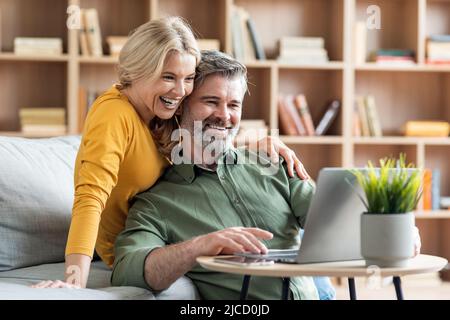 Happy middle aged couple websurfing on laptop together while relaxing at home Stock Photo