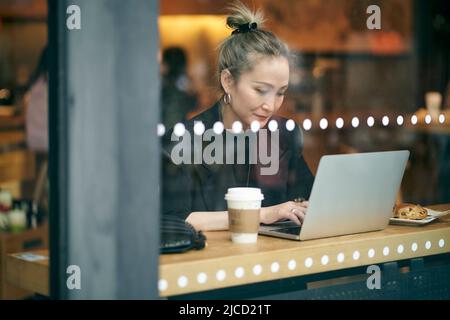 through glass shot of a mid adult asian businesswoman working in coffee shop using laptop computer Stock Photo