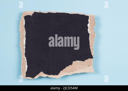 Rectangular piece of black corrugated cardboard with torn edges on light blue background. Top view, copy space Stock Photo