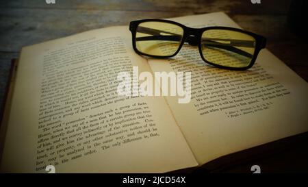 An old book and glasses lie on a wooden table Stock Photo