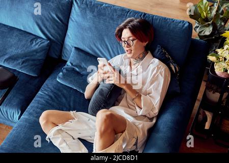 Stylish Asian guy resting on sofa and using smartphone in the living room Stock Photo