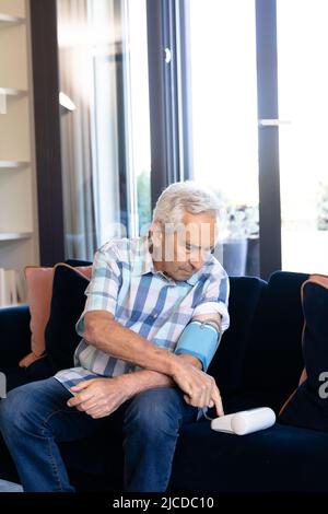 Caucasian senior man checking his blood pressure sitting on the couch at home Stock Photo