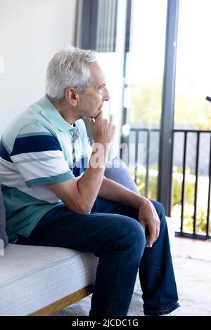 Thoughtful caucasian senior man looking out of the window at home Stock Photo
