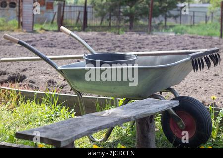 Gray metal garden wheelbarrow with two handles and one wheel. The wheelbarrow is in the garden or garden. Gardener's wheelbarrow in the backyard. Gard Stock Photo