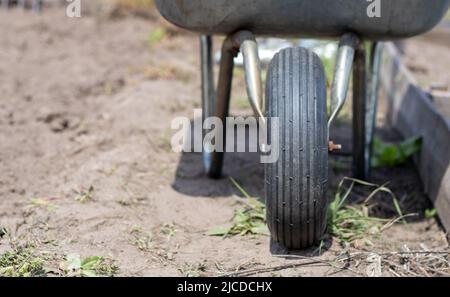 Gray metal garden wheelbarrow with two handles and one wheel. The wheelbarrow is in the garden or garden. Gardener's wheelbarrow in the backyard. Gard Stock Photo