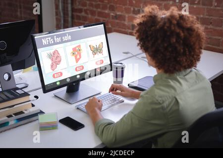 Biracial businessman researching on nfts while working on desktop pc in office Stock Photo
