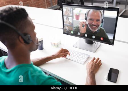 African american businessman discussing with colleagues while video conferencing over computer Stock Photo