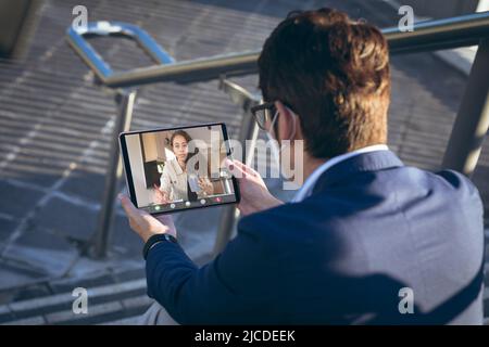 Asian businessman video conferencing with coworker over digital pc while sitting outdoors on steps Stock Photo