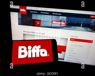 Person holding smartphone with logo of British waste management company Biffa plc on screen in front of website. Focus on phone display. Stock Photo