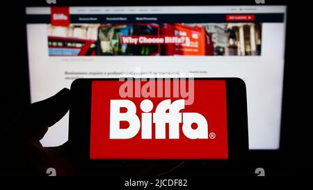 Person holding mobile phone with logo of British waste management company Biffa plc on screen in front of web page. Focus on phone display. Stock Photo