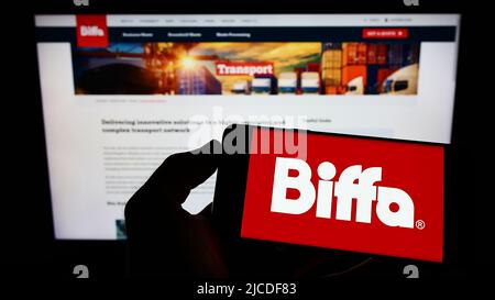 Person holding cellphone with logo of British waste management company Biffa plc on screen in front of business webpage. Focus on phone display. Stock Photo