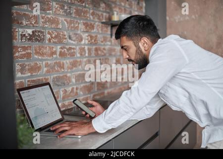 young man using a laptop and a smartphone at the same time. Stock Photo