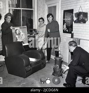 1960s, historical, fire safety education campaign, inside a room, a woman holding an electric fire and a man kneeling down by a small stove, in a picture to highlight fire prevention in the home. A lady is holding a poster warning about the danger of matches..'keep matches away from children', while another poster is on the wall highlighting the importance of fire guards...'  fix that (fire) guard', Fife, Scotland, UK. Stock Photo