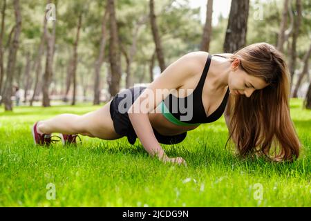 Young fitness woman, stands on push up bars stand, doing plunk