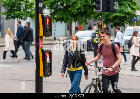 Two people crossing Market St in Manchester UK while a puffin crossing displays 'red man' (do not cross). There are no laws against crossing on red Stock Photo