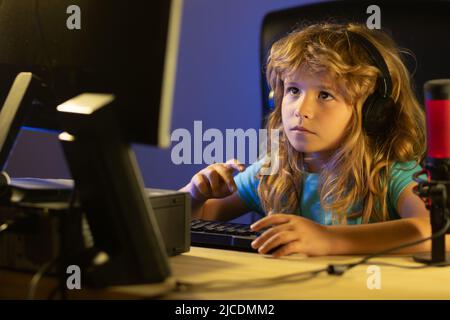 Child plays a video game on the pc computer screen. Portrait of cute child while typing on keyboard. Gamer play computer games. Neon lighting. Stock Photo