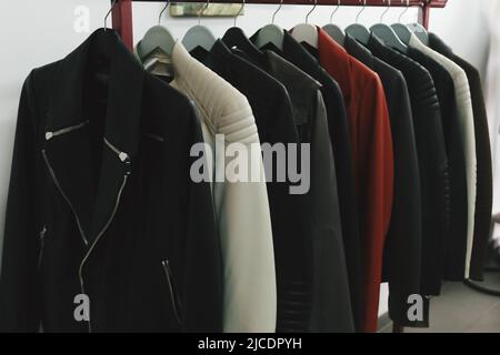 Collection of many new women's leather spring jackets on hangers in the shop. Background and closeup texture of elegant brown, white, black jackets. Stock Photo