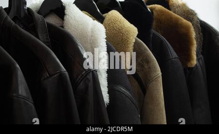 Collection of leather jackets on hangers in the shop. Many new men's winter jackets with fur. Background and closeup texture of leather, Stock Photo