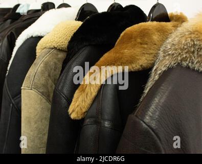 Collection of leather jackets on hangers in the shop. Many new men's winter jackets with fur. Background and closeup texture of leather, Stock Photo