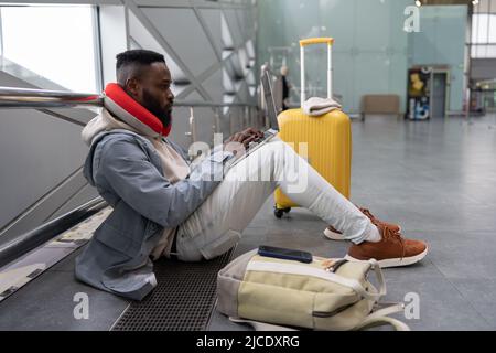 Thoughtful young black male with computer on laps preparing for exam online while waiting flight. Stock Photo
