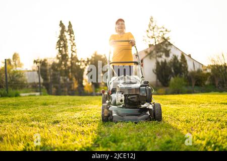 Elderly woman mows the lawn with an electric lawn mower on allotment Stock Photo