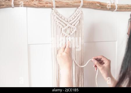 girl weaves a macrame pattern from natural white cotton threads for a large wall panel Stock Photo