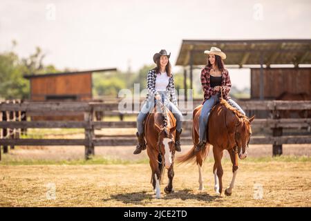 Two cowgirls riding their horses on a ranch during hot summer day. Stock Photo