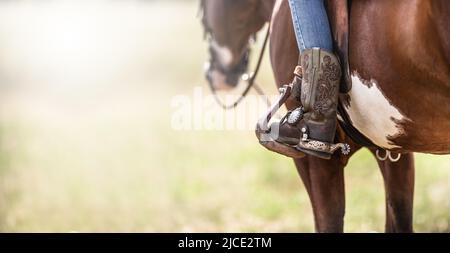 Detail of a ornamented cowboy boots in a stirrup while sitting on a horse. Stock Photo