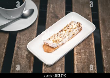 Cup of coffee and eclair on a wooden table close-up. Stock Photo