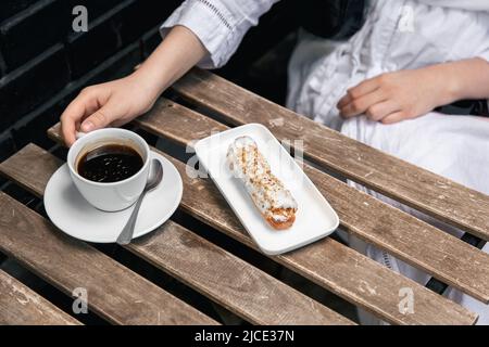 Cup of coffee and eclair on a wooden table close-up. Stock Photo