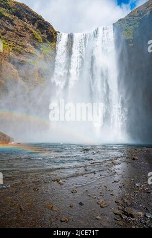 Low angle view of idyllic Skogafoss waterfall falling from cliffs against sky Stock Photo