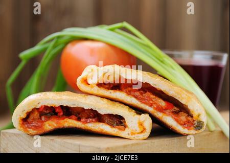 Two pieces of pizza calzone with glass of red wine, fresh scallion and tomato on wooden board closeup macro horizontal Stock Photo