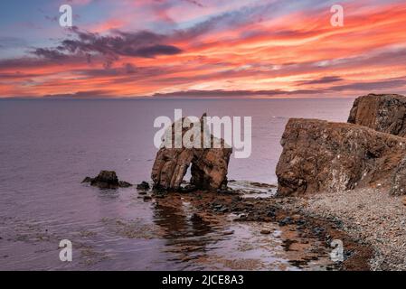 Scenic view of rock formations at seashore against dramatic sky during sunset Stock Photo