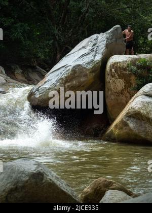 Cisneros, Antioquia, Colombia - February 20, 2022: Water Splash after Man Jumps into River from Huge Rock while others Watch in the Middle of a Forest Stock Photo