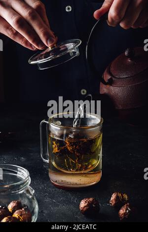 Steeping red tea in glass mug. Pouring boiled water from iron kettle. Stock Photo