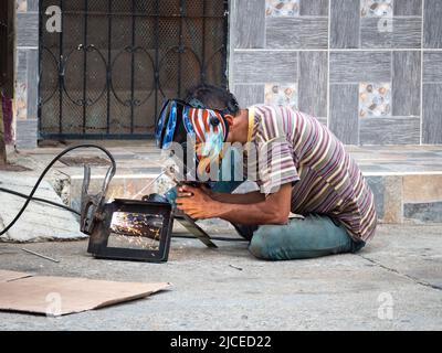 Cisneros, Antioquia, Colombia - February 20, 2022: Man Sitting on the Ground on the Street Welding a Piece of Iron Stock Photo