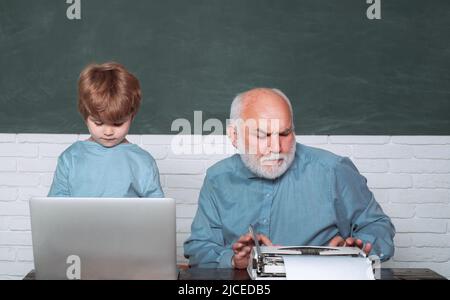 Teacher helping kids with their homework in classroom at school. Dad son are concentrated on the problem. Grandfather and grandson. Tutoring. Stock Photo