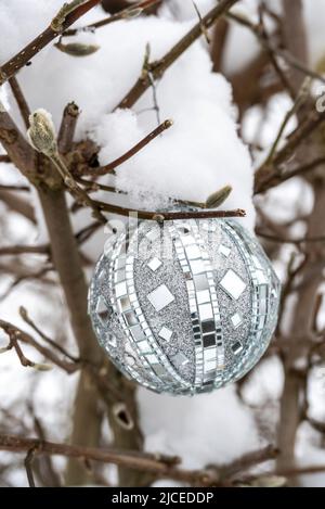silver Christmas ball ornament on an outside tree with snow Stock Photo