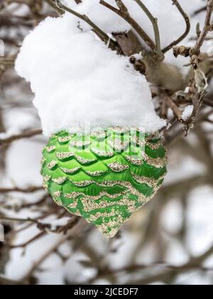 green pine cone Christmas ornament hung on a tree outside covered in snow Stock Photo