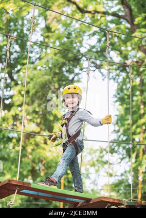 Toddler kindergarten. Active children. Balance beam and rope bridges. Toddler age. Cute child boy. Rope park - climbing center. Helmet and safety Stock Photo