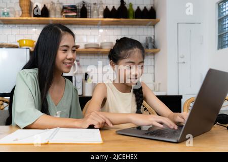 Family and home school concept. Asian mother teach her daughter using application on laptop at home. Stock Photo