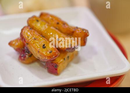Close up sweet Japanese potato or candy potato on a white plate, warm light in the restaurant. Stock Photo