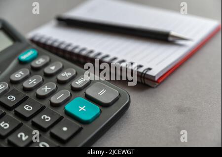 Calculator, pen, notepad lie on a gray surface. Open spring-loaded notebook with blank sheets. Close-up. Stock Photo