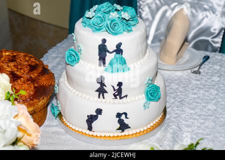 Beautiful wedding cake. White three tier cake with blue roses and figurines of the newlyweds Stock Photo