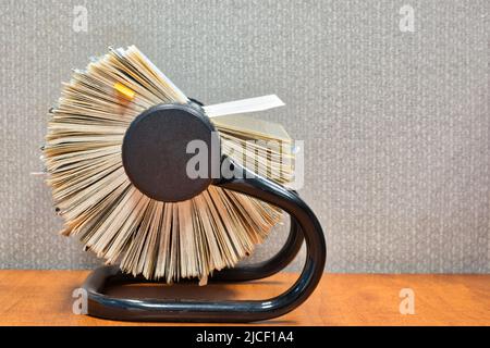 Rolodex file organizer sitting open on an office desk, side view with gray cubicle partition behind. Stock Photo